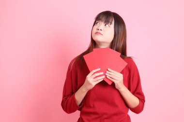 Mutlu Çin Yeni Yılı, pembe arka planda Çin kırmızısı zarflar tutan kırmızı tişörtlü Asyalı bir kadın. Gen Z