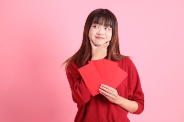 Mutlu Çin Yeni Yılı, pembe arka planda Çin kırmızısı zarflar tutan kırmızı tişörtlü Asyalı bir kadın. Gen Z