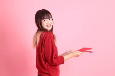 Mutlu Çin Yeni Yılı, pembe arka planda Çin kırmızısı zarflar tutan kırmızı tişörtlü Asyalı bir kadın. Gen Z