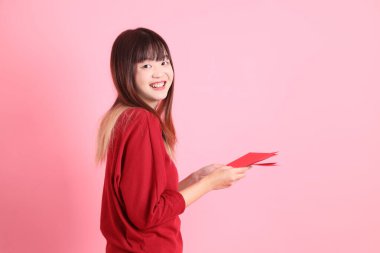 Mutlu Çin Yeni Yılı, pembe arka planda Çin kırmızısı zarflar tutan kırmızı tişörtlü Asyalı bir kadın. Gen Z