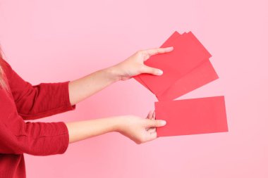 Mutlu Çin Yeni Yılları, pembe arka planda Çin kırmızı zarfları tutan kırmızı tişörtlü Asyalı bir kadının eli.. 