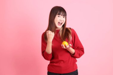 Mutlu Çin Yeni Yılı, kırmızı günlük tişörtlü genç Asyalı kadın elinde Mandalina ya da Portakal jesti ve evet, heyecanlı, pembe arka planda izole edilmiş bir şekilde kutluyor. Gen Z