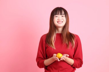 Mutlu Çin Yeni Yılı, pembe arka planda, elinde Mandalina ya da Portakal tutan kırmızı günlük Asyalı kadın tişörtü. Gen Z