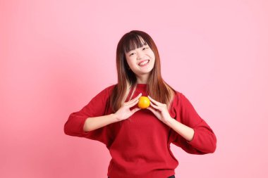 Mutlu Çin Yeni Yılı, pembe arka planda, elinde Mandalina ya da Portakal tutan kırmızı günlük Asyalı kadın tişörtü. Gen Z