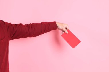 Mutlu Çin Yeni Yılı, resmi ve sıradan kırmızı tişörtlü Asyalı son sınıf öğrencisi pembe arka planda Çin kırmızısı zarflar tutuyor..  