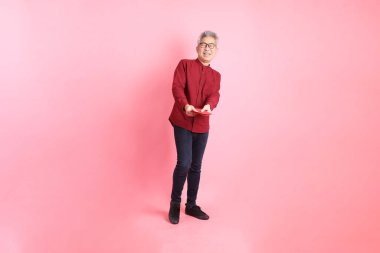 Mutlu Çin Yeni Yılı, resmi ve sıradan kırmızı tişörtlü Asyalı son sınıf öğrencisi pembe arka planda Çin kırmızısı zarflar tutuyor..  