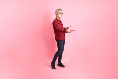 Mutlu Çin Yeni Yılı, resmi ve sıradan kırmızı tişörtlü Asyalı son sınıf öğrencisi pembe arka planda Çin kırmızısı zarflar tutuyor..  