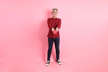 Mutlu Çin Yeni Yılı, resmi ve sıradan kırmızı tişörtlü Asyalı son sınıf öğrencisi pembe arka planda Çin kırmızısı zarflar tutuyor..  