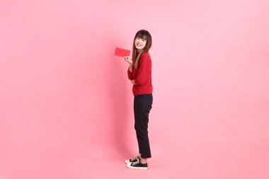 Mutlu Çin Yeni Yılı, pembe arka planda Çin kırmızısı zarflar tutan kırmızı tişörtlü Asyalı bir kadın. Gen Z