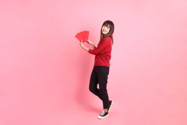 Mutlu Çin Yeni Yılı, pembe arka planda Çin kırmızısı zarflar tutan kırmızı tişörtlü Asyalı bir kadın. Gen Z