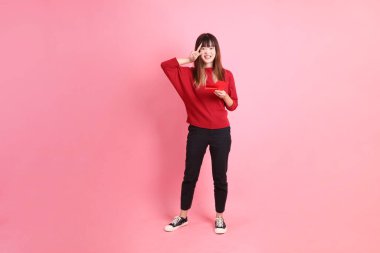 Mutlu Çin Yeni Yılı, kırmızı tişörtlü Asyalı bir kadın elinde Çin kırmızısı zarflar ve pembe arka planda iki parmak ya da Ziyaretçi işareti olan bir jest. Gen Z