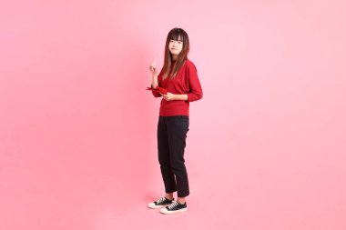 Mutlu Çin Yeni Yılı, kırmızı günlük kırmızı tişörtlü, elinde Çin kırmızısı zarflar tutan Asyalı genç bir kadın pembe arka planda izole edilmiş olmayı reddediyor. Gen Z