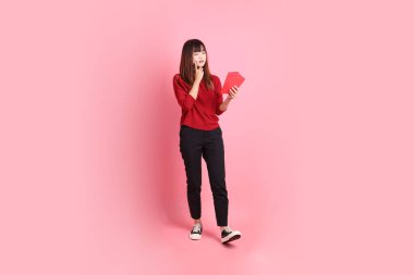 Mutlu Çin Yeni Yılı, kırmızı tişörtlü Asyalı genç bir kadın. Elinde Çin kırmızısı zarflar ve pembe arka planda izole edilmiş bir düşünce var. Gen Z