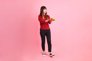 Mutlu Çin Yeni Yılı, pembe arka planda, elinde Mandalina ya da Portakal tutan kırmızı günlük Asyalı kadın tişörtü. Gen Z