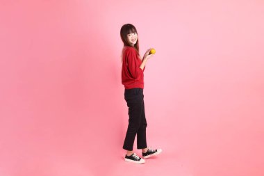 Mutlu Çin Yeni Yılı, pembe arka planda, elinde Mandalina ya da Portakal tutan kırmızı günlük Asyalı kadın tişörtü. Gen Z