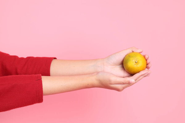 Счастливого китайского Нового года, молодая азиатка в красной повседневной футболке с жестом руки, держащей мандарин или апельсин изолированными на розовом фоне. Gen Z