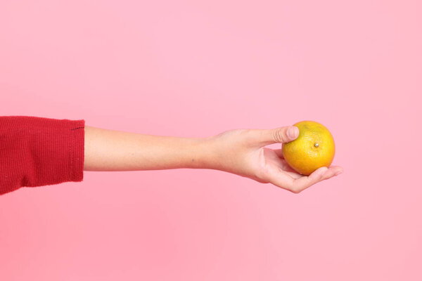 Счастливого китайского Нового года, молодая азиатка в красной повседневной футболке с жестом руки, держащей мандарин или апельсин изолированными на розовом фоне. Gen Z