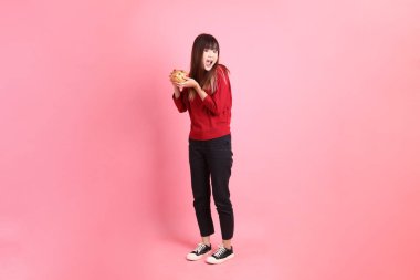 Mutlu Çin Yeni Yılı, kırmızı günlük tişörtlü Asyalı bir kadın altın rengi Çin kumbarası taşıyor pembe arka planda. Gen Z