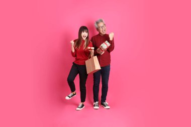 Mutlu Noeller, Asyalı son sınıf ve genç bayan resmi ve günlük kırmızı giysiler içinde, hediye kutusu jesti ile, evet, heyecanlı, pembe arka planda izole edilmiş, kutlanan.