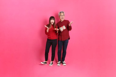 Mutlu Noeller, resmi ve sıradan kırmızı elbiseli Asyalı son sınıf ve genç bayan hediye kutusuyla, sürpriz, pembe arka planda izole edilmiş Wow.