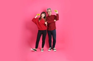 Mutlu Çin Yeni Yılı, Asyalı son sınıf öğrencisi ve genç bayan Noel Baba şapkası ve günlük kırmızı elbiseler giyerler. Pembe arka planda izole edilmiş olarak Mandalina veya Turuncu tutarlar..