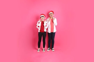 Mutlu Noeller, Asyalı son sınıf öğrencisi ve genç bayan Noel Baba şapkası takın ve beyaz kalp şeklinde tişört giyin sürpriz yapın ve pembe arka planda etkileyici bir şekilde izole olun..