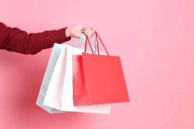 Resmi ve gündelik kırmızı gömlekli Asyalı kıdemli bir adam. Elinde pembe arka planda izole edilmiş çok renkli alışveriş torbalarıyla el ele tutuşuyor..