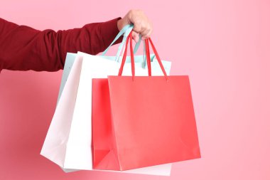 Resmi ve gündelik kırmızı gömlekli Asyalı kıdemli bir adam. Elinde pembe arka planda izole edilmiş çok renkli alışveriş torbalarıyla el ele tutuşuyor..