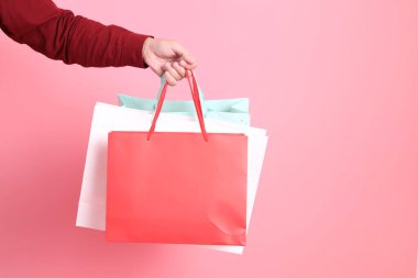 Resmi ve gündelik kırmızı gömlekli Asyalı kıdemli bir adam. Elinde pembe arka planda izole edilmiş çok renkli alışveriş torbalarıyla el ele tutuşuyor..