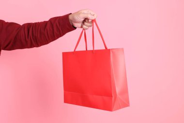 Resmi ve gündelik kırmızı tişörtlü Asyalı son sınıf öğrencisi pembe arka planda izole edilmiş kırmızı alışveriş çantasıyla el ele tutuşuyor..