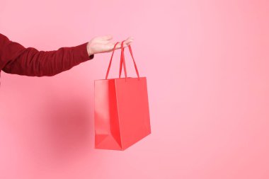 Resmi ve gündelik kırmızı tişörtlü Asyalı son sınıf öğrencisi pembe arka planda izole edilmiş kırmızı alışveriş çantasıyla el ele tutuşuyor..
