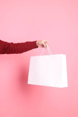 Resmi ve gündelik kırmızı tişörtlü Asyalı kıdemli bir adam pembe arka planda izole edilmiş beyaz bir alışveriş çantasıyla el ele tutuşuyor..