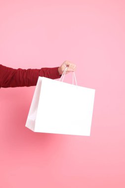 Resmi ve gündelik kırmızı tişörtlü Asyalı kıdemli bir adam pembe arka planda izole edilmiş beyaz bir alışveriş çantasıyla el ele tutuşuyor..