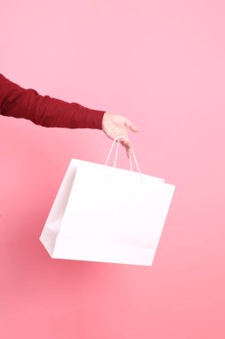 Resmi ve gündelik kırmızı tişörtlü Asyalı kıdemli bir adam pembe arka planda izole edilmiş beyaz bir alışveriş çantasıyla el ele tutuşuyor..