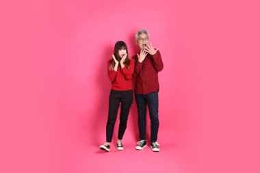 Çin Yeni Yılı, Asyalı son sınıf öğrencisi erkek ve kadın Noel Baba şapkası giyer, sürpriz jestli gündelik kırmızı kıyafetler giyer, vay ve etkileyici, pembe arka planda izole edilmiş..