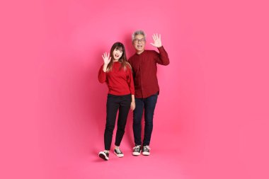 Çin Yeni Yılı, Asyalı son sınıf öğrencisi erkek ve kadın Noel Baba şapkası giyerler, işaret eden kırmızı kıyafetler giyerler, selamlama, davet ya da hoş geldin, pembe arka planda izole edilmiş..