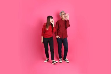 Çin Yeni Yılı, Asyalı son sınıf öğrencisi erkek ve kadın Noel Baba şapkası giyerler, kırmızı günlük kıyafetler giyerler ve pembe arka planda izole bir şekilde bağırırlar..