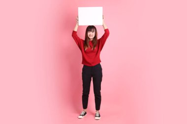 Çin Yeni Yılı, pembe arka planda boş tuval tutan kırmızı, sıradan tişörtlü Asyalı bir kadın. Gen Z