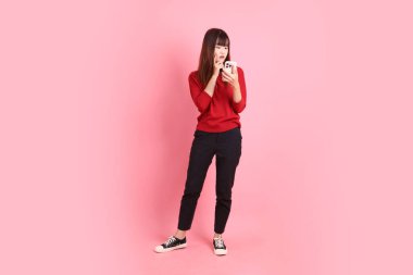 Mutlu Çin Yeni Yılları, pembe arka planda izole edilmiş, el ele tutuşan, kırmızı, sıradan tişörtlü Asyalı genç bayan. Gen Z