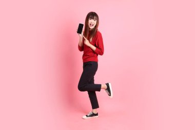 Mutlu Çin Yeni Yılları, pembe arka planda izole edilmiş, el ele tutuşan cep telefonu jesti ile kırmızı günlük Asyalı kadın tişörtü. Gen Z