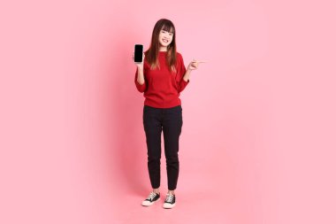 Mutlu Çin Yeni Yılları, pembe arka planda izole edilmiş, el ele tutuşan cep telefonu jesti ile kırmızı günlük Asyalı kadın tişörtü. Gen Z