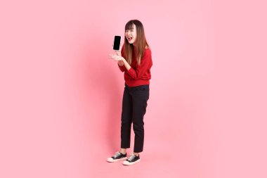 Mutlu Çin Yeni Yılları, pembe arka planda izole edilmiş, el ele tutuşan cep telefonu jesti ile kırmızı günlük Asyalı kadın tişörtü. Gen Z