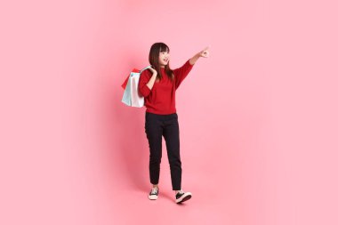 Mutlu Çin Yeni Yılı, pembe arka planda izole edilmiş, el ele tutuşan, kırmızı, sıradan tişörtlü, Asyalı bir kadın. Gen Z