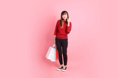 Mutlu Çin Yeni Yılı, kırmızı günlük tişörtlü Asyalı genç bayan alışveriş çantası jesti ve pembe arka planda izole edilmiş selamlama. Gen Z