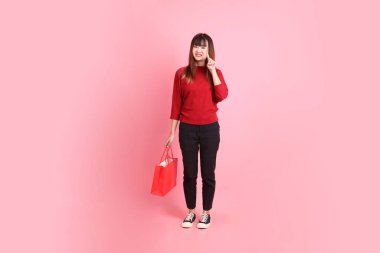 Mutlu Çin Yeni Yılı, pembe arka planda izole edilmiş, el ele tutuşan, kırmızı, sıradan tişörtlü, Asyalı bir kadın. Gen Z