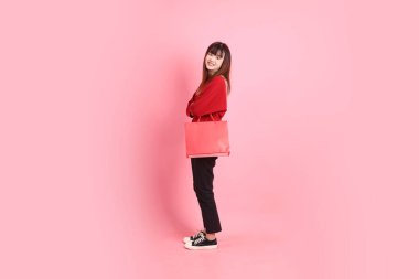 Mutlu Çin Yeni Yılı, pembe arka planda izole edilmiş el ele tutuşan kırmızı tişörtlü Asyalı kadın. Gen Z