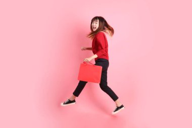 Mutlu Çin Yeni Yılı, kırmızı günlük tişörtlü, el ele tutuşan, pembe arka planda izole edilmiş bir şekilde atlayan Asyalı bir kadın. Gen Z