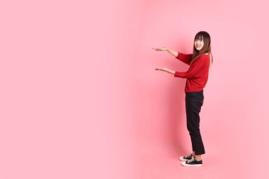 Mutlu Çin Yeni Yılı, kırmızı günlük tişörtlü Asyalı genç bayan işaret eden, selamlayan, pembe arka planda izole edilmiş bir davetiye. Gen Z