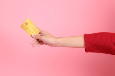 Mutlu Çin Yeni Yılı, kırmızı günlük tişörtlü Asyalı genç bir kadın el ele tutuşup pembe arka planda izole edilmiş kırmızı kredi kartı kullanıyor. Gen Z