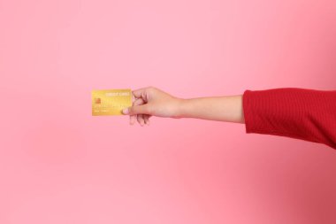 Mutlu Çin Yeni Yılı, kırmızı günlük tişörtlü Asyalı genç bir kadın el ele tutuşup pembe arka planda izole edilmiş kırmızı kredi kartı kullanıyor. Gen Z